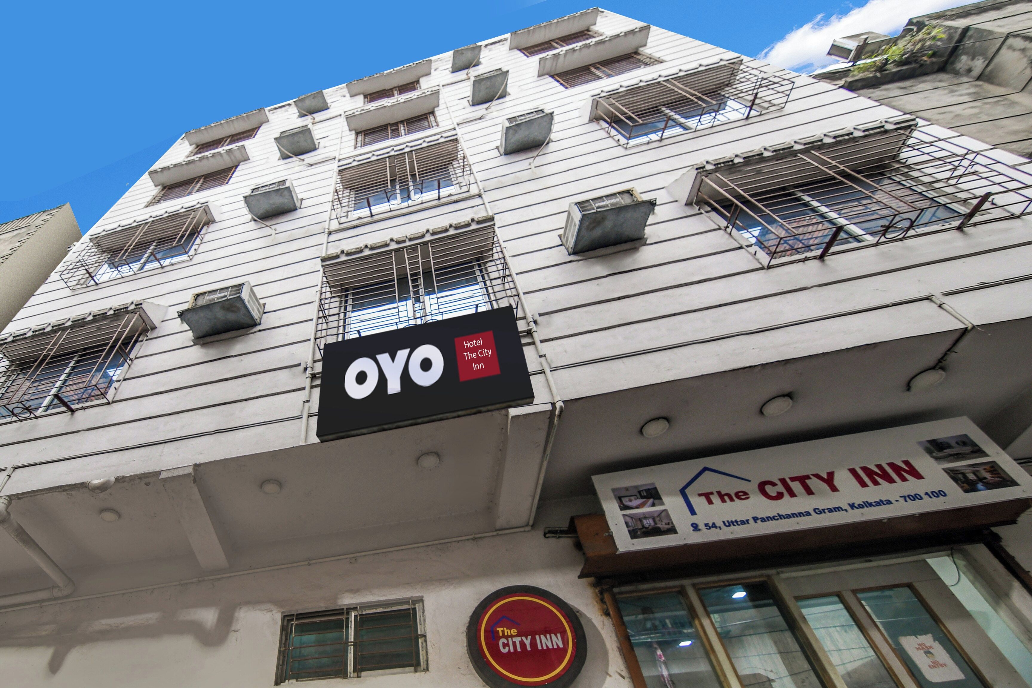 A building with multiple air conditioning units, a sign for 'OYO Hotel The City Inn,' and a sign for 'The City Inn' with an address.
