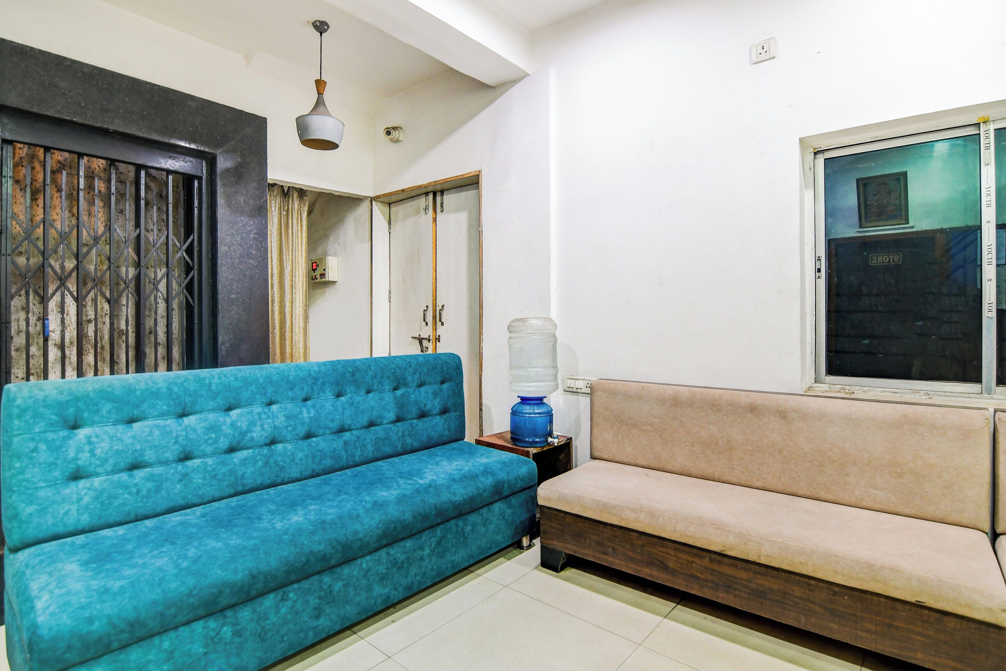 Una stanza con un divano blu, un divano beige, un distributore d'acqua, una lampada a soffitto e una porta con inferriata metallica.