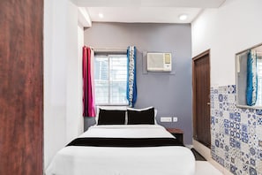 A bedroom with a bed, a window with curtains, an air conditioning unit, and a tiled wall. - Hotel O CITY INN (Kolkata)