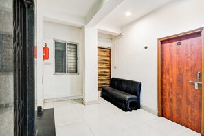 A hallway with a black bench, a wooden door, and a window with a fire extinguisher. - Hotel O CITY INN (Kolkata)