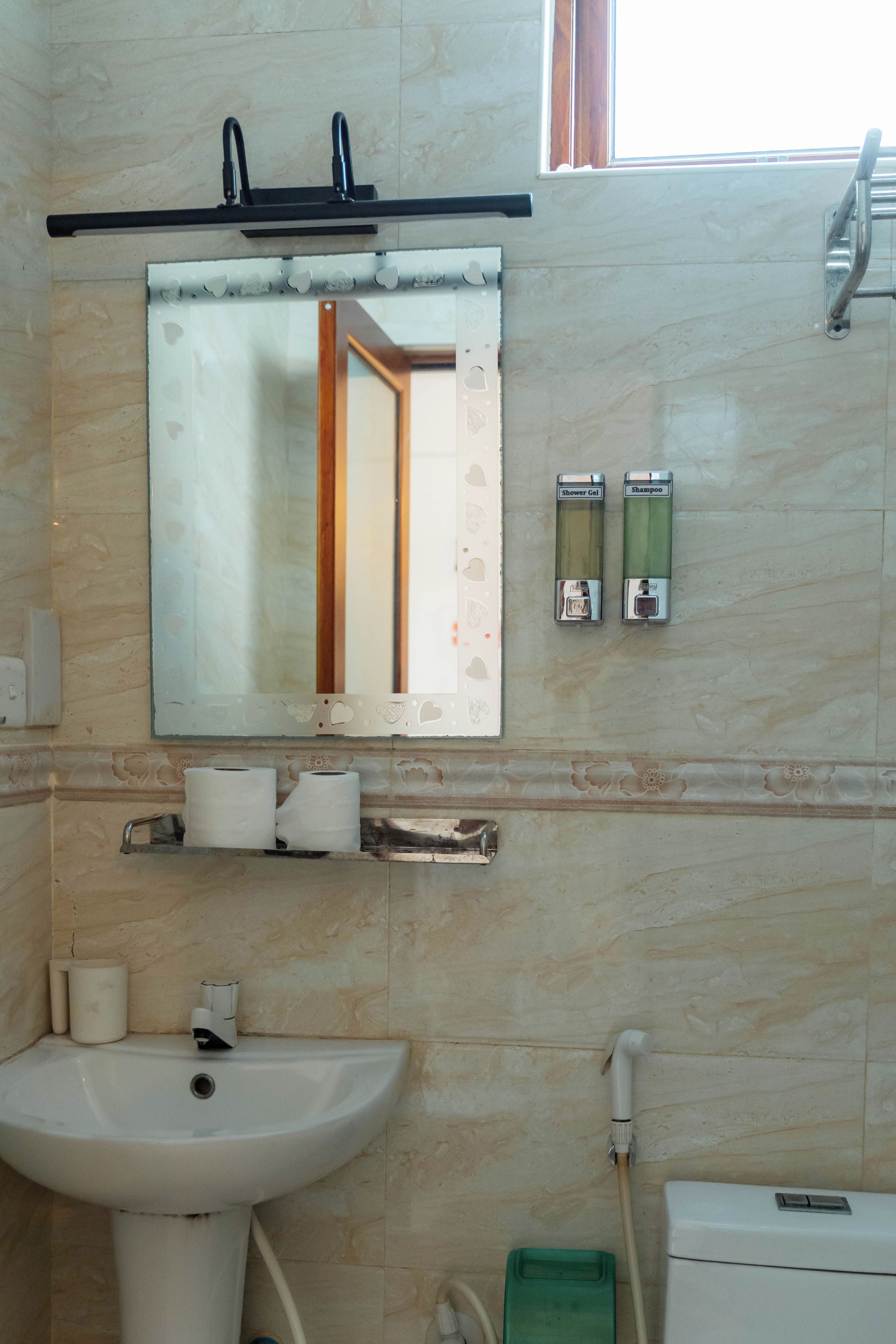 Un baño con lavamanos, espejo, dispensador de toallas y soporte para papel higiénico.