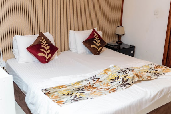 A hotel room with a bed, pillows, a nightstand, a lamp, and a power outlet. - Naaboli Inn (Hulhumale)