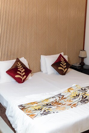 Una habitación de hotel con cama, almohadas, mesita de noche y lámpara.