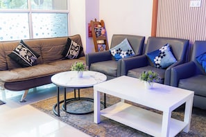 A living room with a brown sofa, two armchairs, a white coffee table, and a patterned rug. - Naaboli Inn (Hulhumale)
