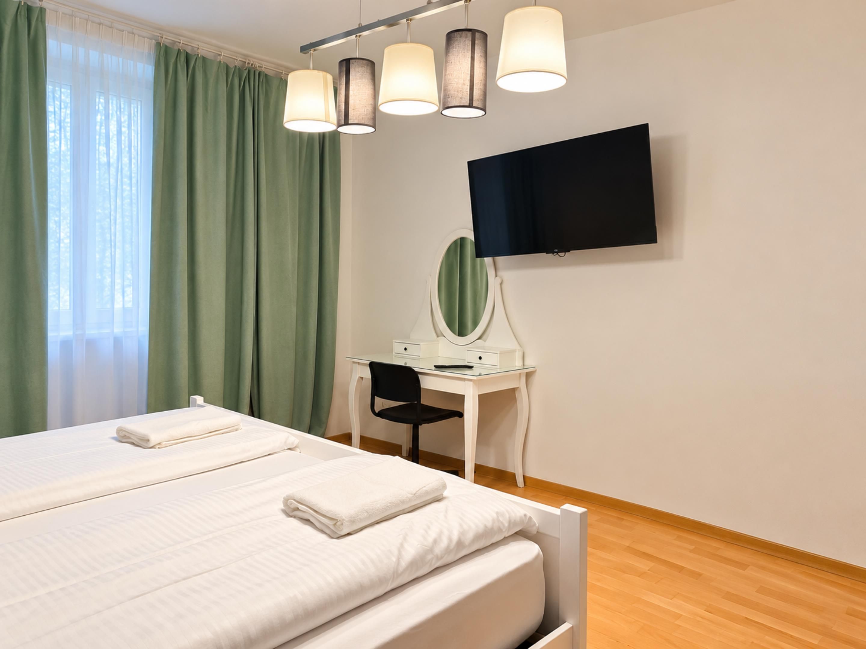 Et hotelværelse med en seng, et skrivebord med et spejl og et fladskærms-tv på væggen.