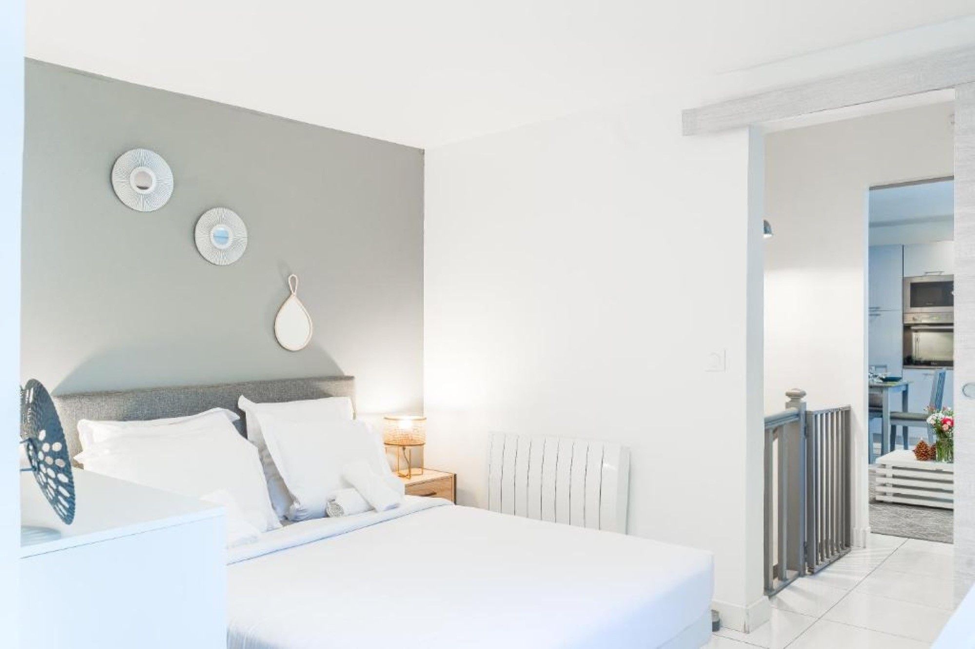 Habitación de hotel con cama, mesita de noche, lámpara y vista al área de la cocina.