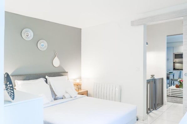 Habitación de hotel con cama, mesita de noche, lámpara y vista al área de la cocina.