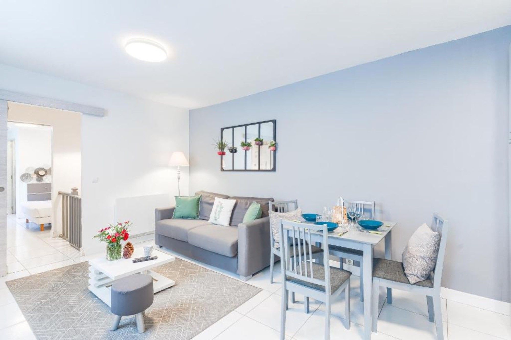 Un salon moderne avec un canapé gris, une table à manger avec des chaises et une table basse blanche.