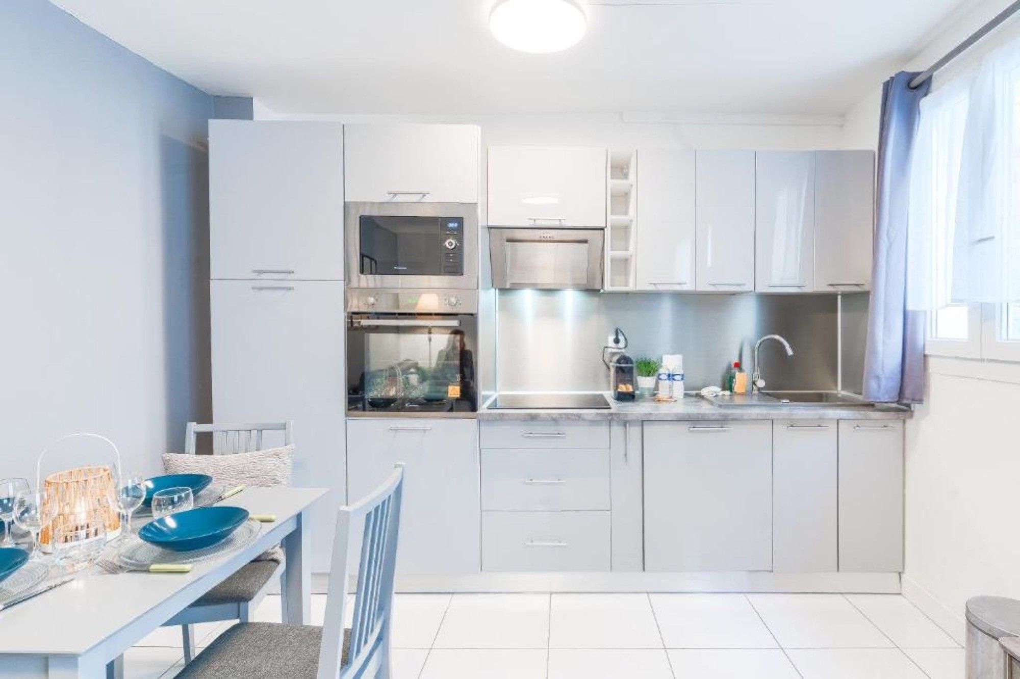 Una cocina moderna con armarios blancos, electrodomésticos de acero inoxidable y una zona de comedor con una mesa preparada para dos.