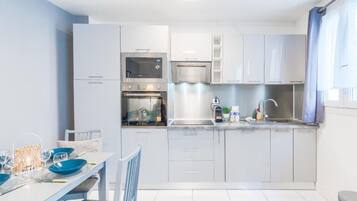 Una cocina moderna con armarios blancos, electrodomésticos de acero inoxidable y una zona de comedor con una mesa preparada para dos.