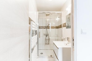 Un baño estrecho con cabina de ducha de vidrio, un lavamanos blanco y un espejo.