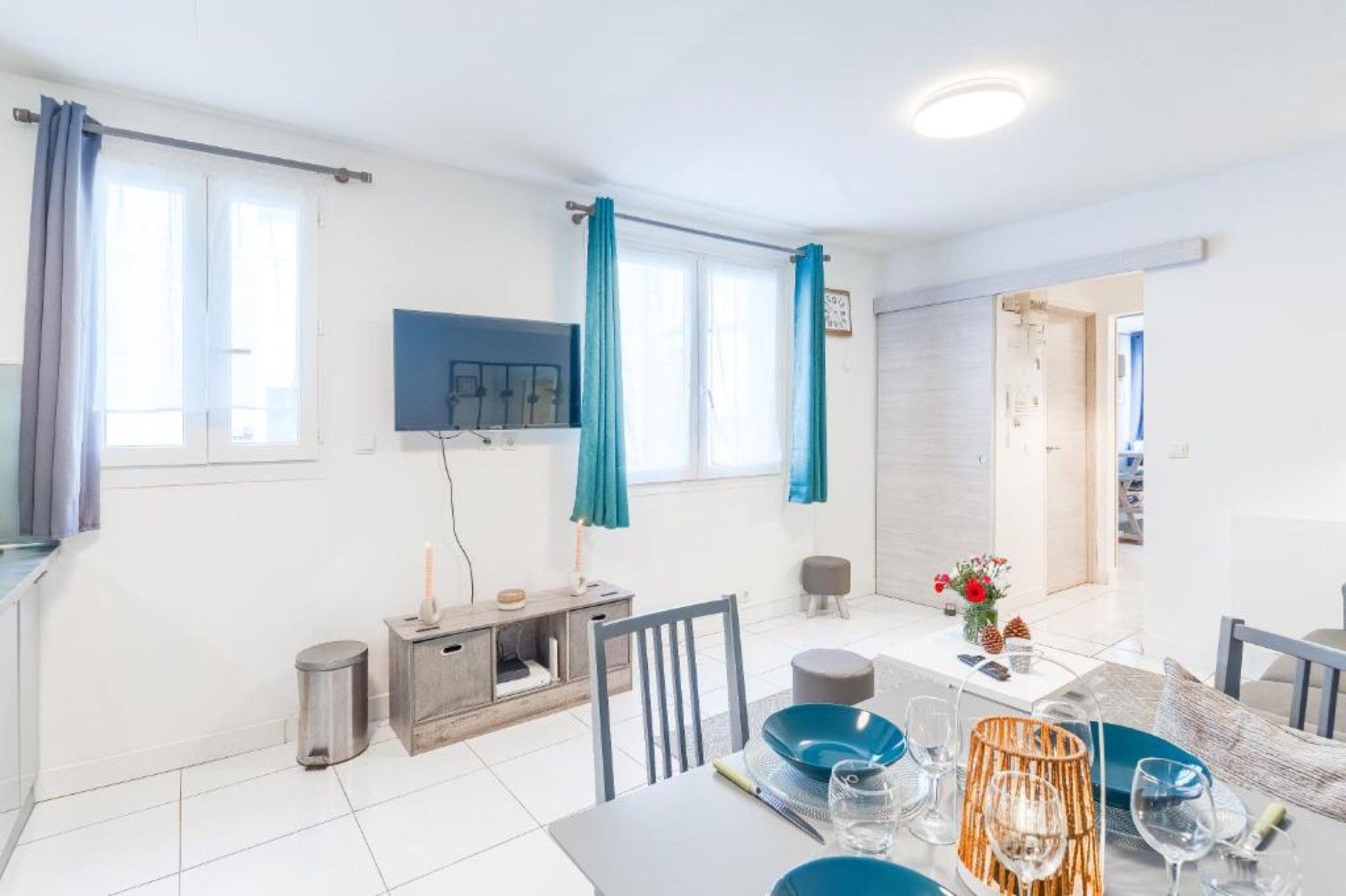 Un comedor moderno con una mesa dispuesta para dos, un televisor montado en la pared y vistas al exterior a través de amplios ventanales.