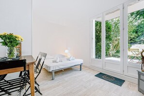 A room with a bed, a table with chairs, a vase with flowers, and a view of greenery through a glass door. - Apartment 'Le Jardin Canisy - Piscine - Tennis' with Shared Pool, Private Terrace and Wi-Fi (Saint-Arnoult)