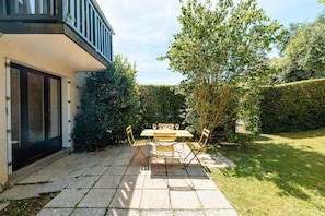 A patio with a table and chairs, a building with a balcony, and a well-maintained hedge. - Apartment 'Le Jardin Canisy - Piscine - Tennis' with Shared Pool, Private Terrace and Wi-Fi (Saint-Arnoult)