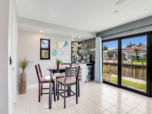 A modern kitchen with a dining area, large windows, and a view of a canal. - Gulf Access Water View Home, No Bridges, 1 Block access to Caloosahatchee River (Cape Coral)