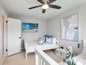 Un dormitorio con cama, escritorio, ventilador de techo, una pintura de playa y un cuadro abstracto grande.