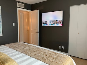 A bedroom with a bed, a television mounted on the wall displaying various channels, a closed door, and a wall-mounted air vent. - Updated Old Town 1st Fl Parking Pool Spa Hot Tub (Scottsdale)