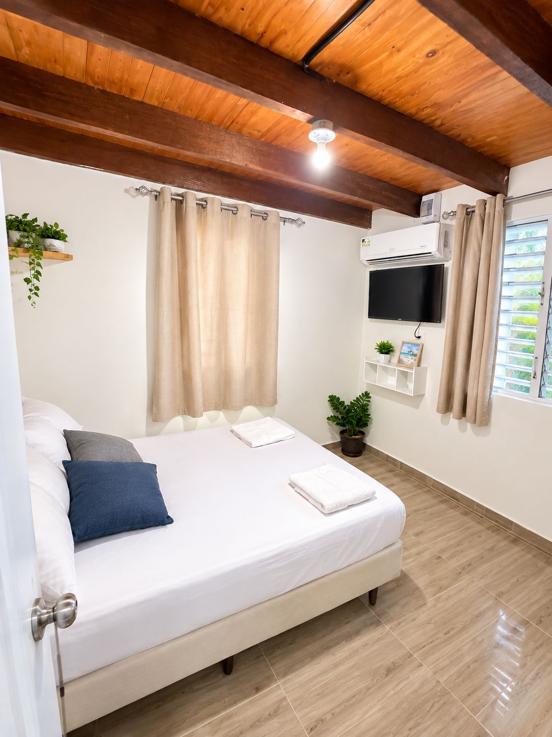 Une chambre à coucher avec un lit, des rideaux, un téléviseur fixé au mur et une fenêtre également dotée de rideaux.