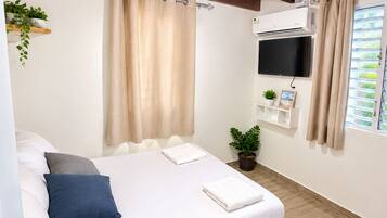Une chambre à coucher avec un lit, des rideaux, un téléviseur fixé au mur et une fenêtre également dotée de rideaux.