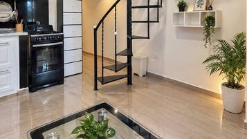 A modern kitchen with a black stove, white cabinets, and a black spiral staircase.
