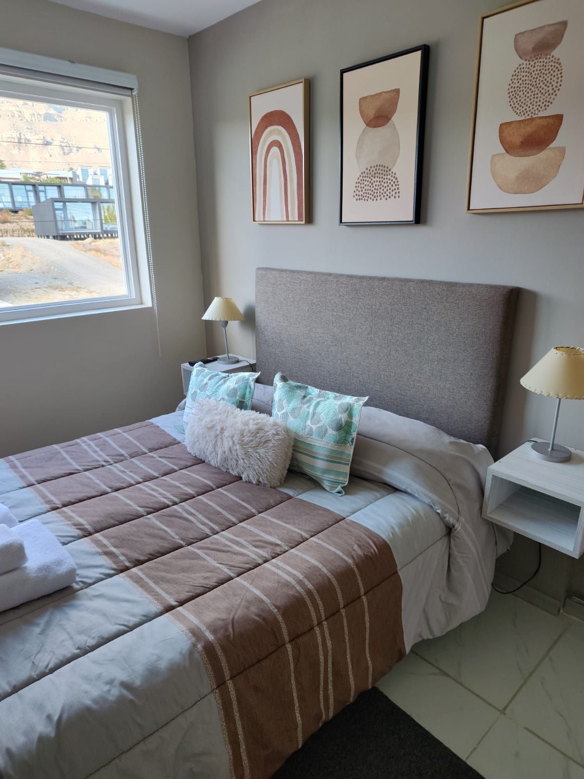 A bedroom with a bed, pillows, a nightstand, a lamp, and artwork on the wall.