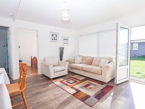 A modern living room with a beige sofa, a wooden chair, and a patterned rug. - 122 Norton Park (Dartmouth)