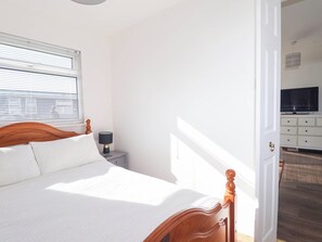 A bedroom with a wooden bed, a bedside table with a lamp, a TV in the adjacent room, and a door leading to another room. - 122 Norton Park (Dartmouth)