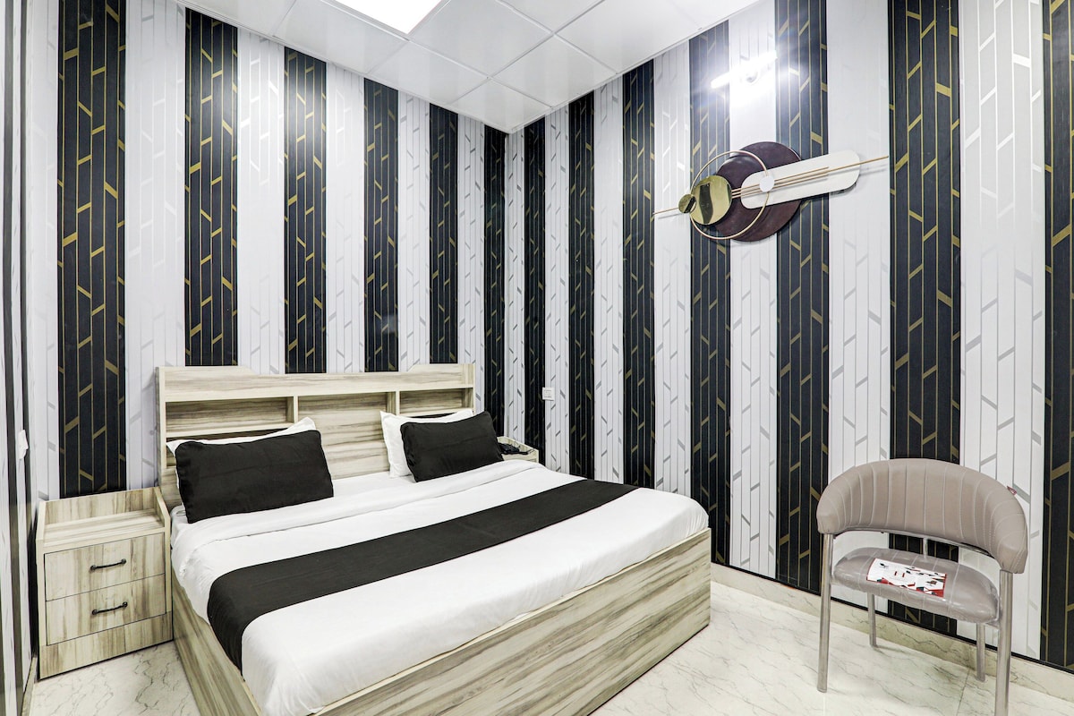 Habitació d'hotel amb llit, taules de nit, una cadira i aire condicionat fixat a la paret.