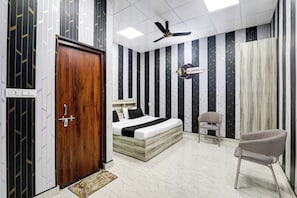 A bedroom with a bed, a chair, a ceiling fan, and a door. - Hotel O Mansa Lawn & Banquets (Lucknow)
