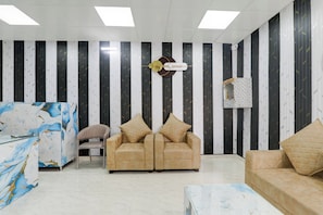 A modern living room with striped wallpaper, a marble-patterned coffee table, and two beige sofas with cushions. - Hotel O Mansa Lawn & Banquets (Lucknow)