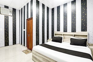 A bedroom with a bed, a wooden door, and a wall with vertical stripes. - Hotel O Mansa Lawn & Banquets (Lucknow)