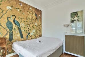 A bedroom with a large wall mural of peacocks, a bed, a side table, and a framed picture on the wall. - Elegant Parisian Apartment minutes from Trocadero – Passy, 16th Arrondissement (Paris)