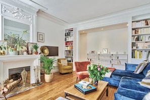 A spacious living room with a fireplace, a bookshelf, a blue sofa, and a coffee table. - Elegant Parisian Apartment minutes from Trocadero – Passy, 16th Arrondissement (Paris)