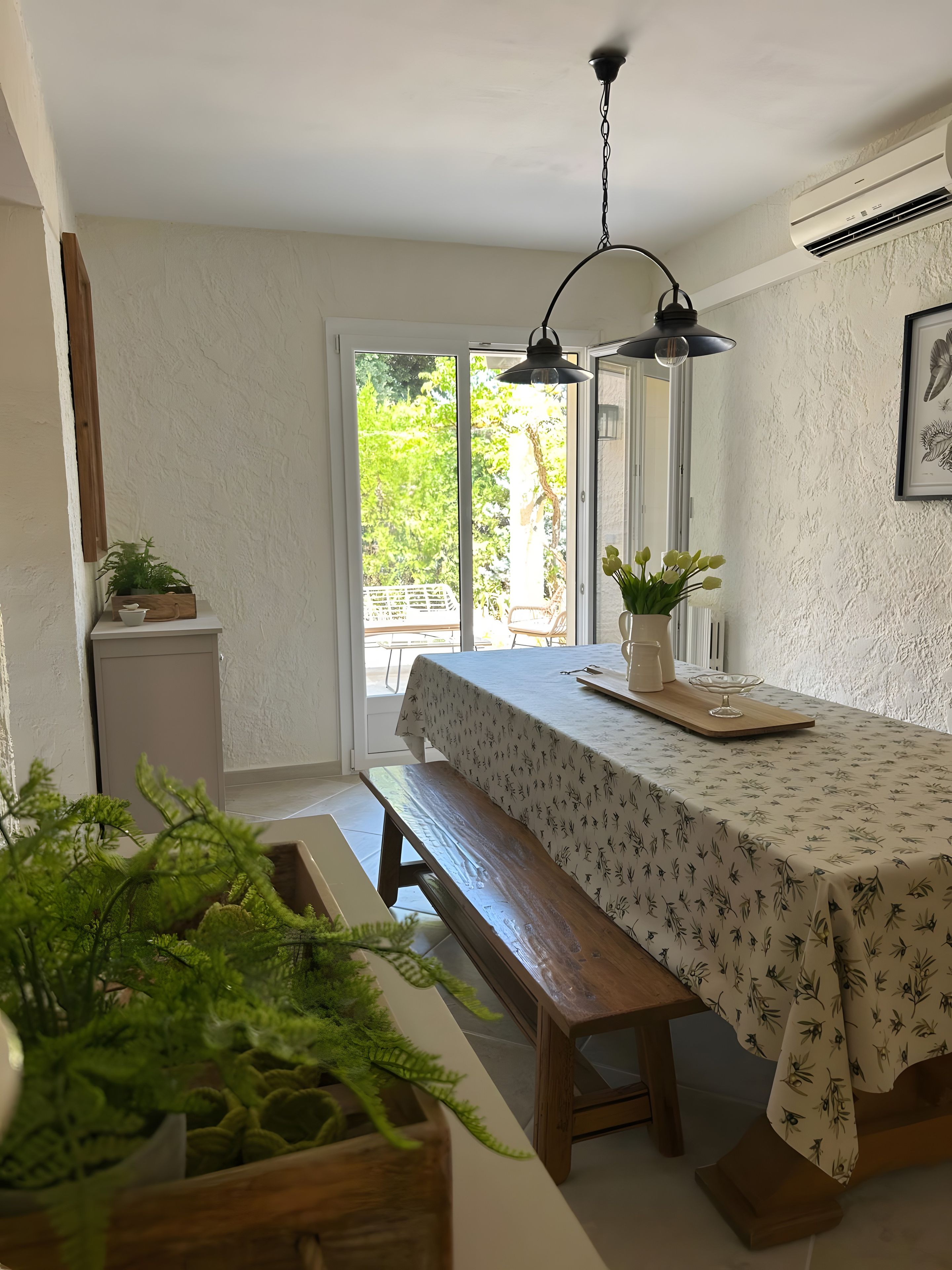 Un coin repas avec une table dressée pour deux personnes, un banc et une vue sur l’extérieur.