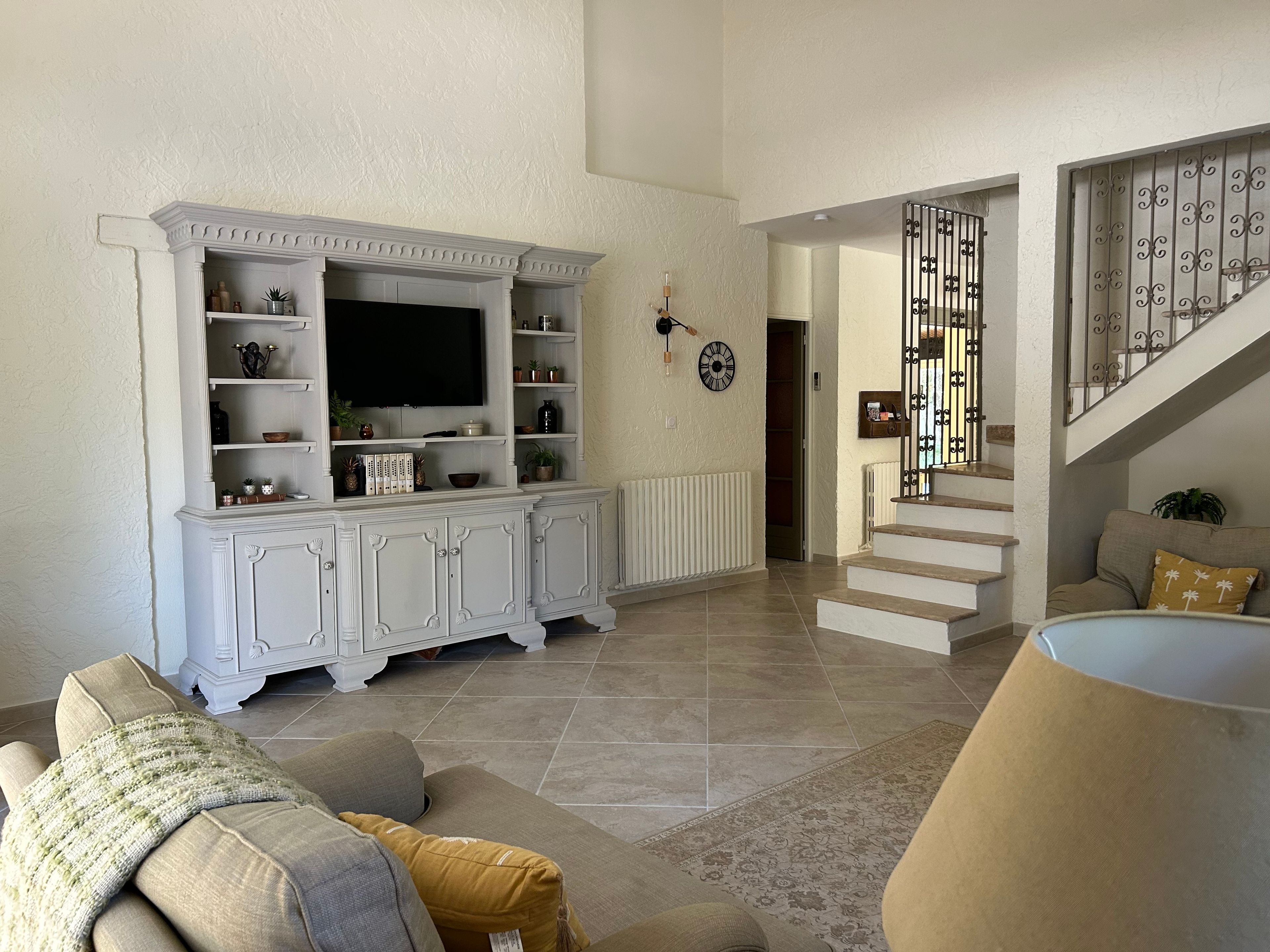 Un salon avec un meuble de rangement blanc pour les appareils électroniques, un escalier et un canapé avec des coussins.