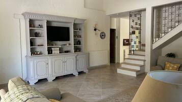 Un salon avec un meuble de rangement blanc pour les appareils électroniques, un escalier et un canapé avec des coussins.