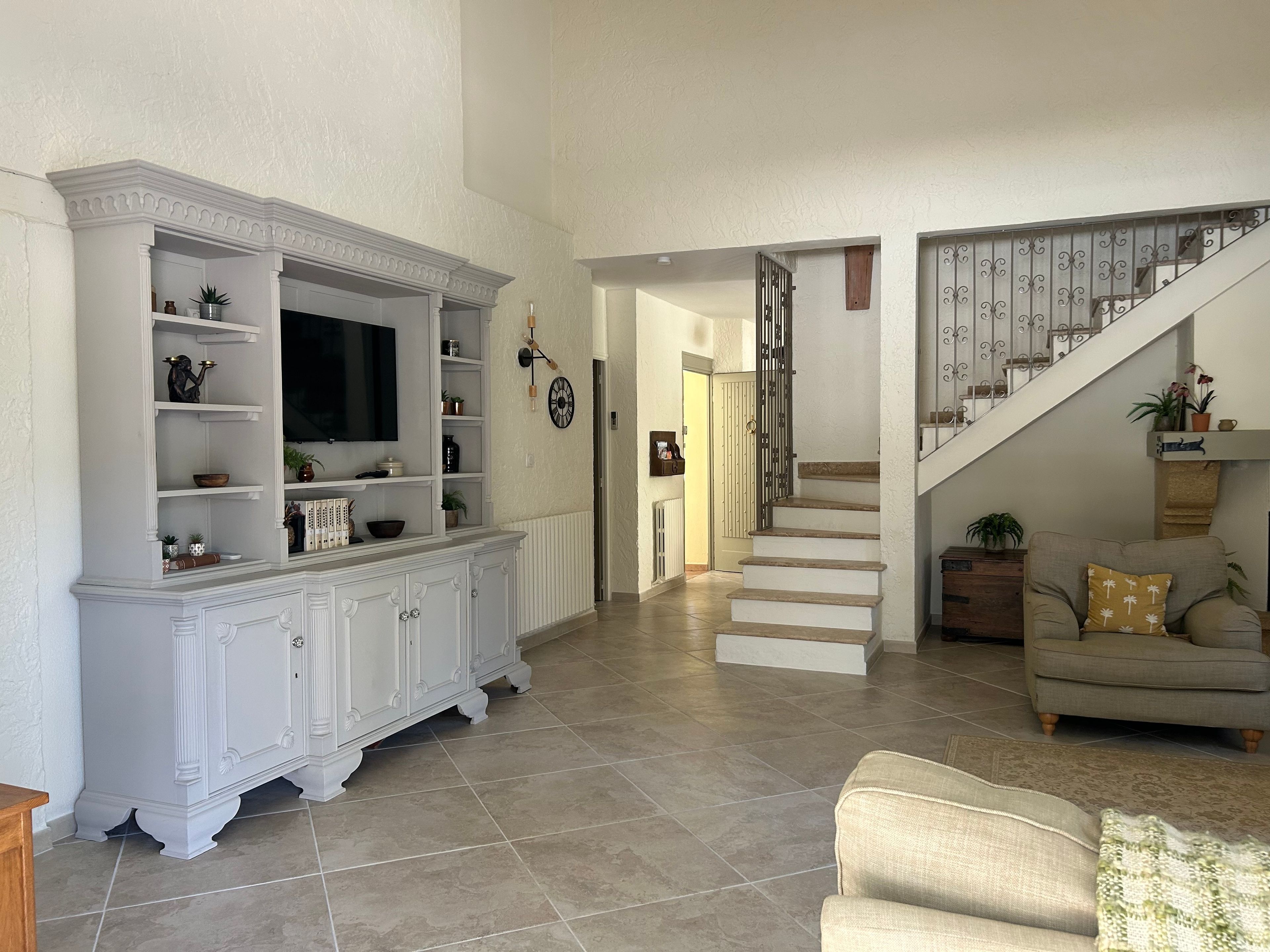 Un vaste espace de vie comprenant un meuble de rangement blanc pour les appareils multimédias, un escalier et un canapé beige.