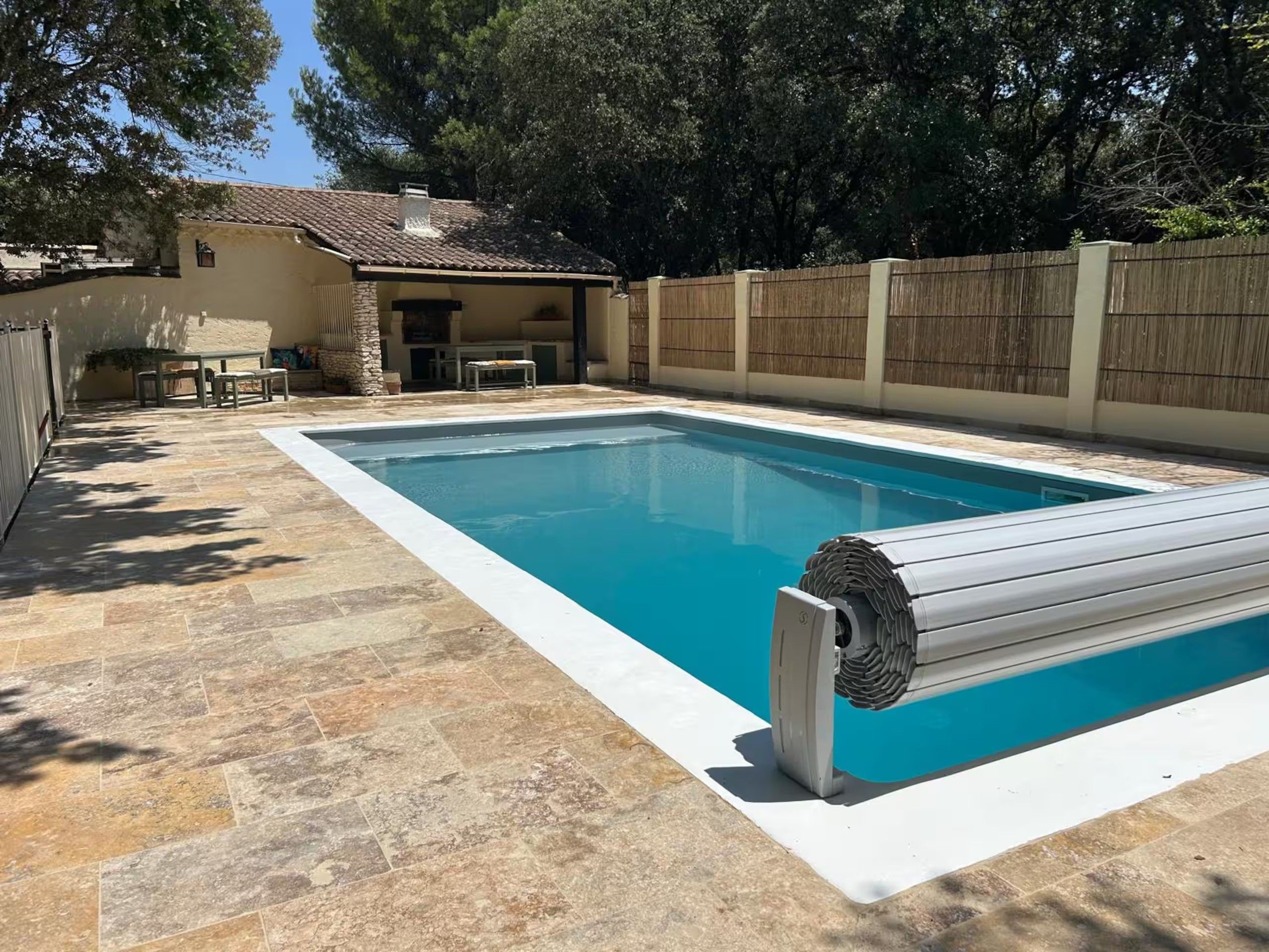 Une piscine avec une terrasse carrelée et une chaise longue en bois.