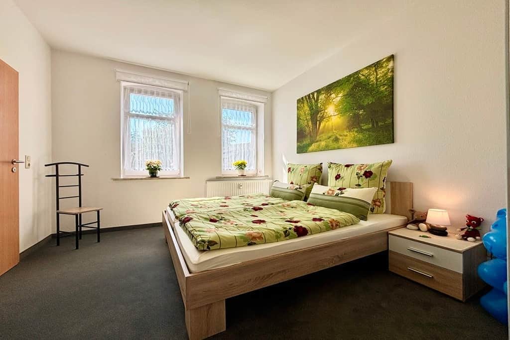 Ein Schlafzimmer mit Bett, Nachttisch, Schminktisch, Fenster und einem Bild an der Wand.