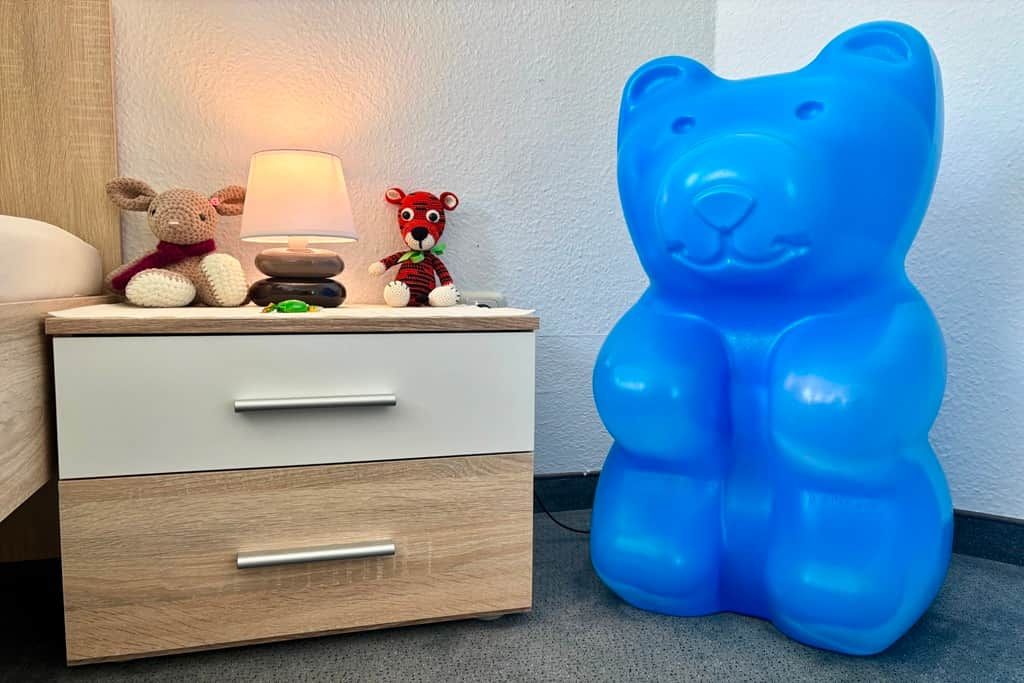 Een nachtkastje met een lamp, twee knuffelberen en een blauw beertje-vormig object.