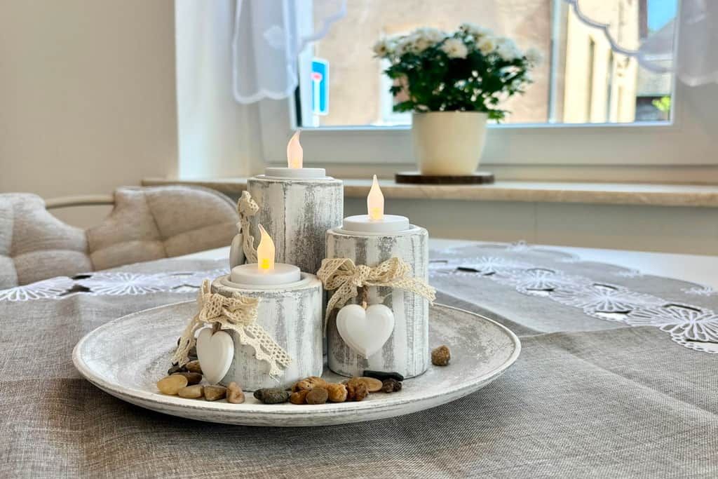 Una bandeja con velas sobre un mantel texturizado, rodeada de piedras decorativas y un adorno con forma de corazón.