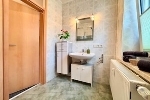 A bathroom with a wooden door, a white cabinet, a sink with a mirror above it, and a radiator. - Grossi's Haamit-Stüb'l (Schneeberg)