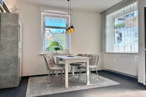 A dining area with a table and chairs, a hanging light fixture, a window with a view of greenery, and a radiator. - Grossi's Haamit-Stüb'l (Schneeberg)
