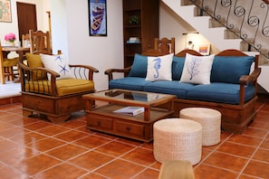 A cozy living room with wooden furniture, a glass coffee table, and a staircase with a wrought iron railing. - Beautiful 5-bedroom Colonial house with pool in Historic Centro Mérida (Mérida)