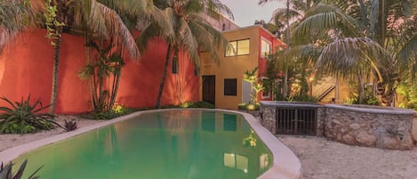 A swimming pool with a curved edge, surrounded by a sandy area and palm trees.