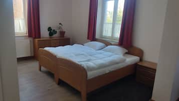 Un dormitorio con cama de madera, una mesita de noche, un radiador, una ventana con cortinas y una planta en maceta.