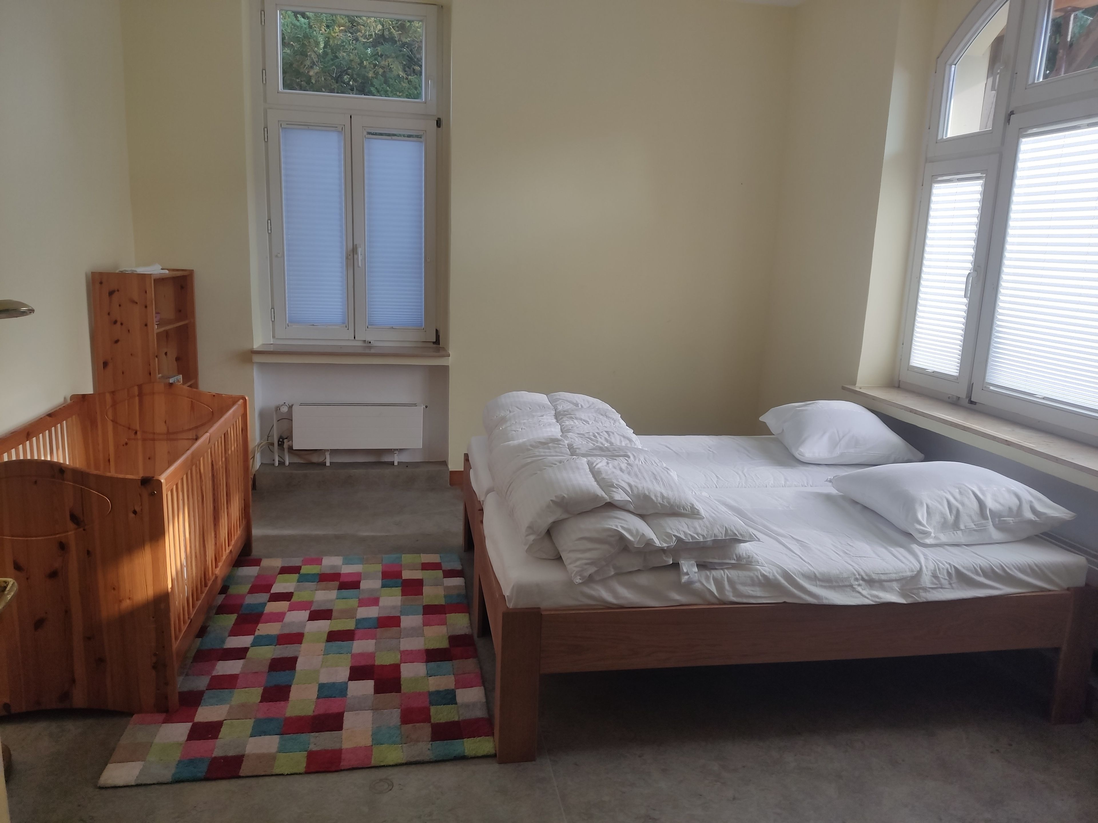 A bedroom with a bed, a crib, a window, and a radiator.