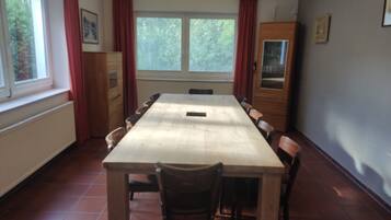 A dining room with a long table, chairs, a cabinet, and windows with curtains.