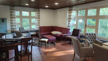 Una sala de estar con un sofá seccional rojo, una mesa de comedor con sillas y ventanas grandes con cortinas.