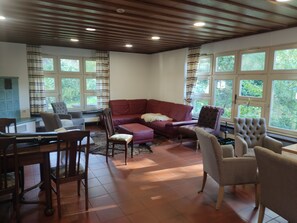 Un salon avec un canapé d’angle rouge, une table à manger avec des chaises et de grandes fenêtres avec des rideaux.